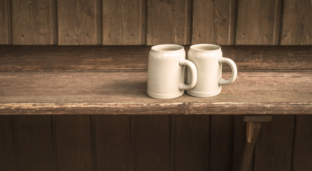 Two bavarian style beer mugs in front of a wooden backgroundの写真素材