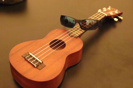 Ukulele and sunglasses lay on a dark table