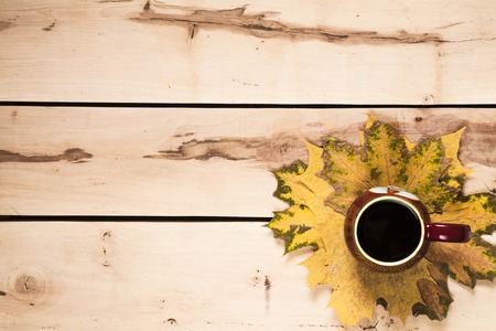Cup of coffee with autumn leaves on the wooden backgroundの写真素材
