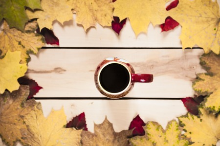 Cup of coffee with autumn leaves on the wooden backgroundの写真素材