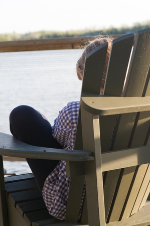 Teenage girl sitting in an Adirondack chair, Lake of the Woods, Ontario, Canadaの写真素材