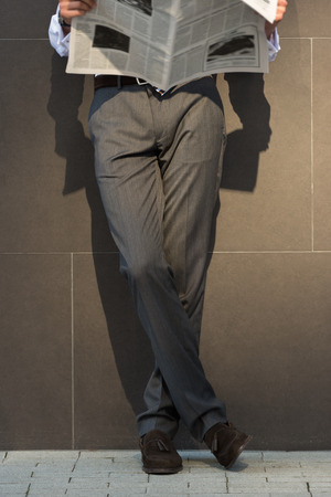 Business man reading a newspaper on the street leaning on wall of modern buildingの写真素材