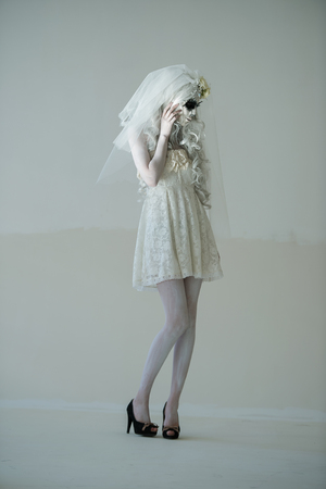 Halloween witch. Beautiful woman wearing santa muerte mask and wedding dress posing full lengthの写真素材