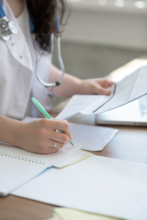 Female doctor taking notes during looking at patient medical tests at her officeの写真素材