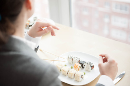 Young businesswoman eats sushi in formal dressの写真素材