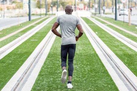 Back view of black man running in urban background. Male doing workout outdoors.