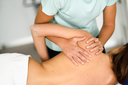 Professional female physiotherapist giving shoulder massage to brunette woman in hospital. Medical check at the shoulder in a physiotherapy center.の写真素材