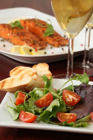 Mixed greens with cherry tomatoes and bread. Wine and smoked salmon in backgroundの写真素材