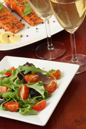 Mixed greens with cherry tomatoes. Wine and smoked salmon in backgroundの写真素材