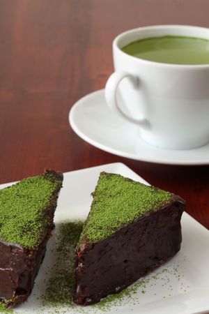 Chocolate cake garnished with Matcha green tea powder and a cup of green teaの写真素材