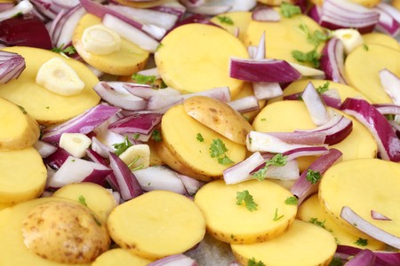 Raw potatoes with red onion, garlic and parsley on a baking tray, ready to be put into the ovenの写真素材