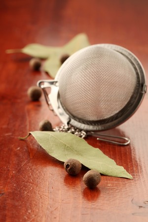 Allspice, bay leaf and tea strainer on a wooden backgroundの写真素材