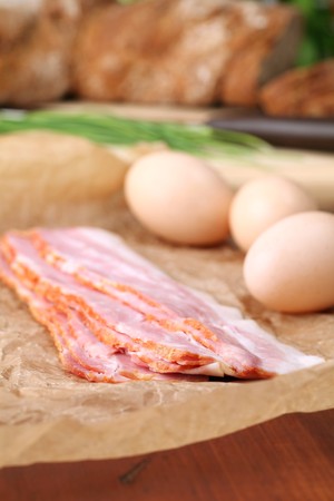 Bacon and eggs on waxed paper with chives and bread in the background. Ingredients for delicious...