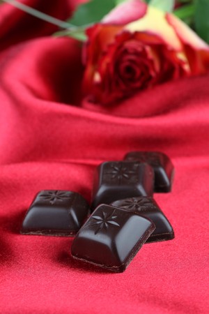 Chocolate and rose on red satin backgroundの写真素材
