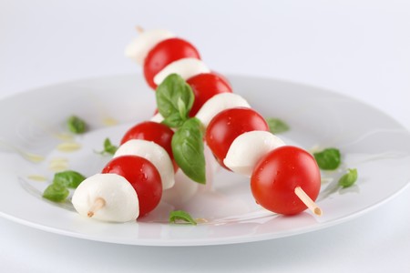 Caprese salad. Cherry tomatoes and mozzarella on skewers, garnished with basil leaves and olive oilの写真素材
