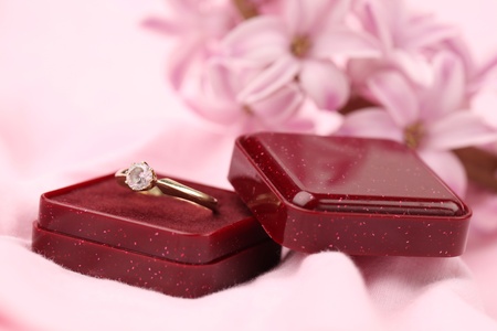 Gold engagement ring with diamond in a red box. Pink hyacinth in background. Shallow dof