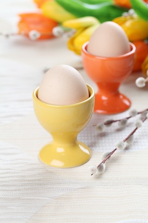 Eggs in orange and yellow eggcups with tulips and catkins in backgroundの写真素材