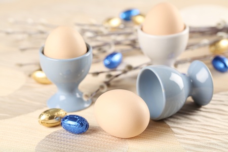 Eggs in white and blue eggcups with catkins and little chocolate eggs in foilの写真素材