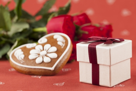 Little gift box with gingerbread heart and red roses in backgroundの写真素材
