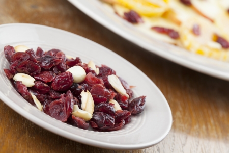 Dried cranberries and roasted almonds on a plate and fruit salad in backgroundの写真素材