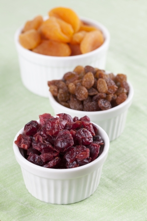 Dried raisins, cranberries and apricots in white bowlsの写真素材