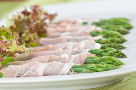 Prosciutto wrapped green asparagus with lollo rosso lettuce on a plateの写真素材