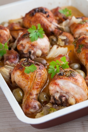 Roast chicken drumsticks with green olives and onion on a baking sheetの写真素材