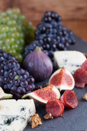 Slate board with blue cheese, blue and green grapes, figs, walnuts and salamiの写真素材