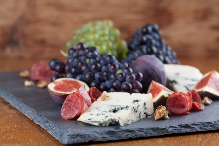 Slate board with blue cheese, blue and green grapes, figs, walnuts and salamiの写真素材