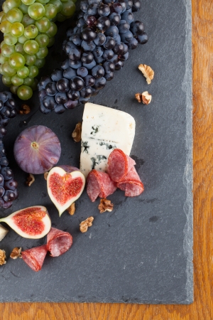 Slate board with blue cheese, blue and green grapes, figs, walnuts and salamiの写真素材