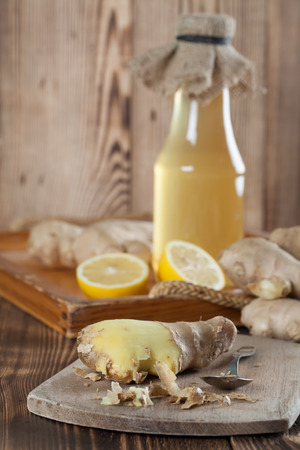 Peeled ginger root with lemons and a bottle of ginger syrup in background. Shallow dofの写真素材