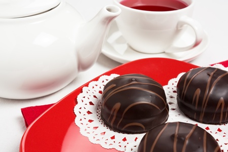 Delicious three chocolate cake on red plate with tea cup and teapot の写真素材
