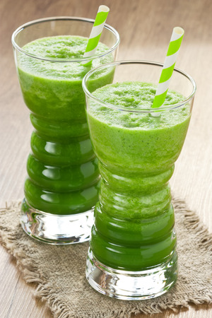 Spinach and green apple smoothie in two glass with straw on wooden backgroundの写真素材