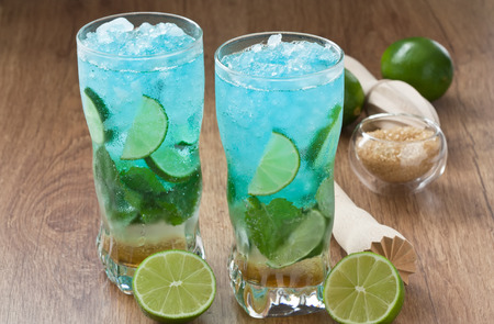 Blue mojito cocktail refreshing summer drink with lime, mint and ice on rustic wooden tableの写真素材