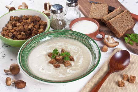 Creamy mushroom soup in bowl with fried croutons, parsley and brown bread on white background
の写真素材