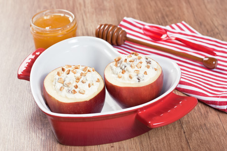 Baked apple stuffed cream cheese, raisins, almonds, honey in red casserole dish in form heart on wooden background
の写真素材