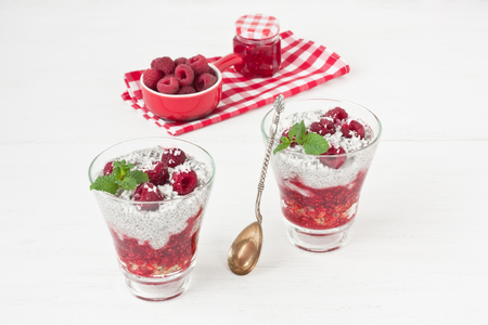 Chia seeds coconut milk pudding with oatmeal granola, raspberry jam, coconut chips and mint in glass on white wooden backgroundの写真素材