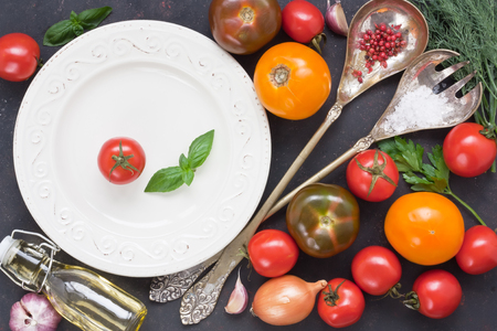 Assortment fresh colorful tomato and vegetable for salad with white plate, tableware vintage spoon and fork on black rustic backgroundの写真素材