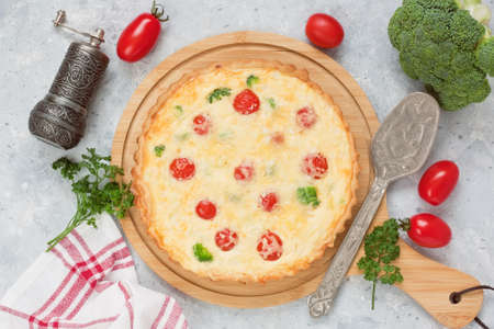 Quiche pie with broccoli, cherry tomatoes, salmon fish, cheese, eggs with cream on wooden cutting...