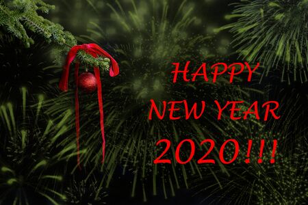 New Year 2020 greetings card. A fir tree branch with a red ribbon and a glitter ball. Fireworks effects on a dark background.の写真素材