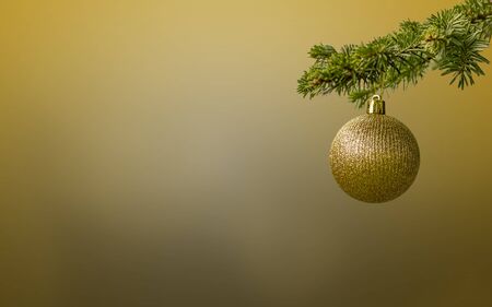 Fir tree branch with a golden glitter ball on golden flat background. Bokeh effects. Christmastime. Christmas postcard.の写真素材