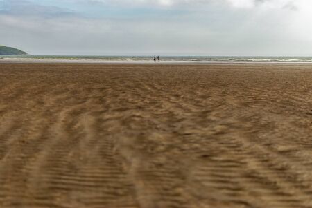 Couple walking on sandy beach leaving footprints in the sand. One father and his daughter enjoying the day. Cloudy day.の写真素材