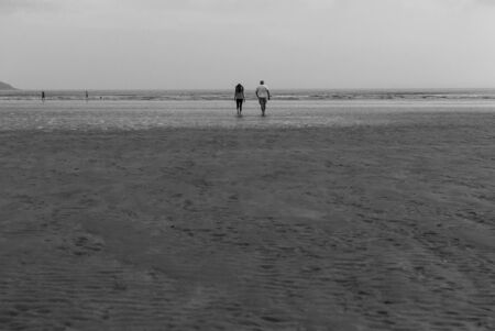 Couple walking on sandy beach leaving footprints in the sand. One father and his daughter enjoying the day. Cloudy day.の写真素材