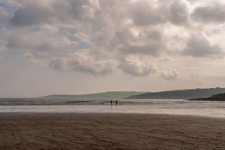 Couple walking on sandy beach leaving footprints in the sand. One father and his daughter enjoying the day. Cloudy day.の写真素材