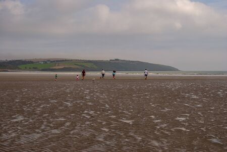 People walking on sandy beach leaving footprints in the sand. Family with children and a dog playing on Killbrittain beach, Ireland. Cloudy day.の写真素材