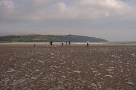 People walking on sandy beach leaving footprints in the sand. Family with children and a dog playing on Killbrittain beach, Ireland. Cloudy day.の写真素材
