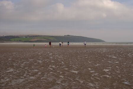 People walking on sandy beach leaving footprints in the sand. Family with children and a dog playing on Killbrittain beach, Ireland. Cloudy day.の写真素材