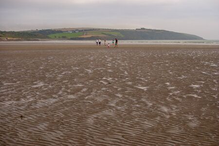 People walking on sandy beach leaving footprints in the sand. Family with children and a dog playing on Killbrittain beach, Ireland. Cloudy day.の写真素材