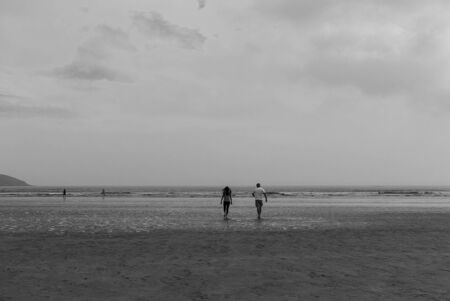 Couple walking on sandy beach leaving footprints in the sand. One father and his daughter enjoying the day. Cloudy day.の写真素材