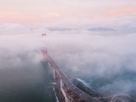 Aerial sunset aerial view of the Golden Gate bridge in San Francisco above the clouds. Romantic panoramic view with clouds flying over the bridge.の写真素材